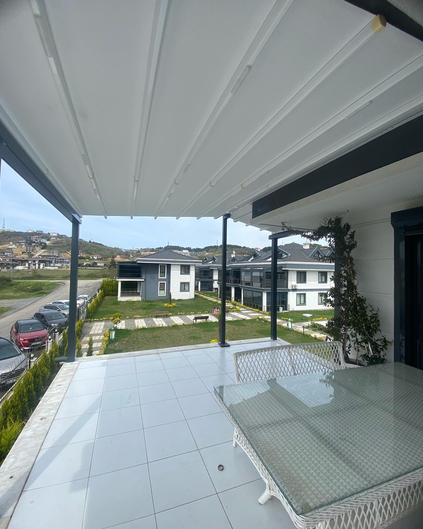 Rolling roof pergola altından bahçe manzarası — açık pozisyon, beyaz lamel